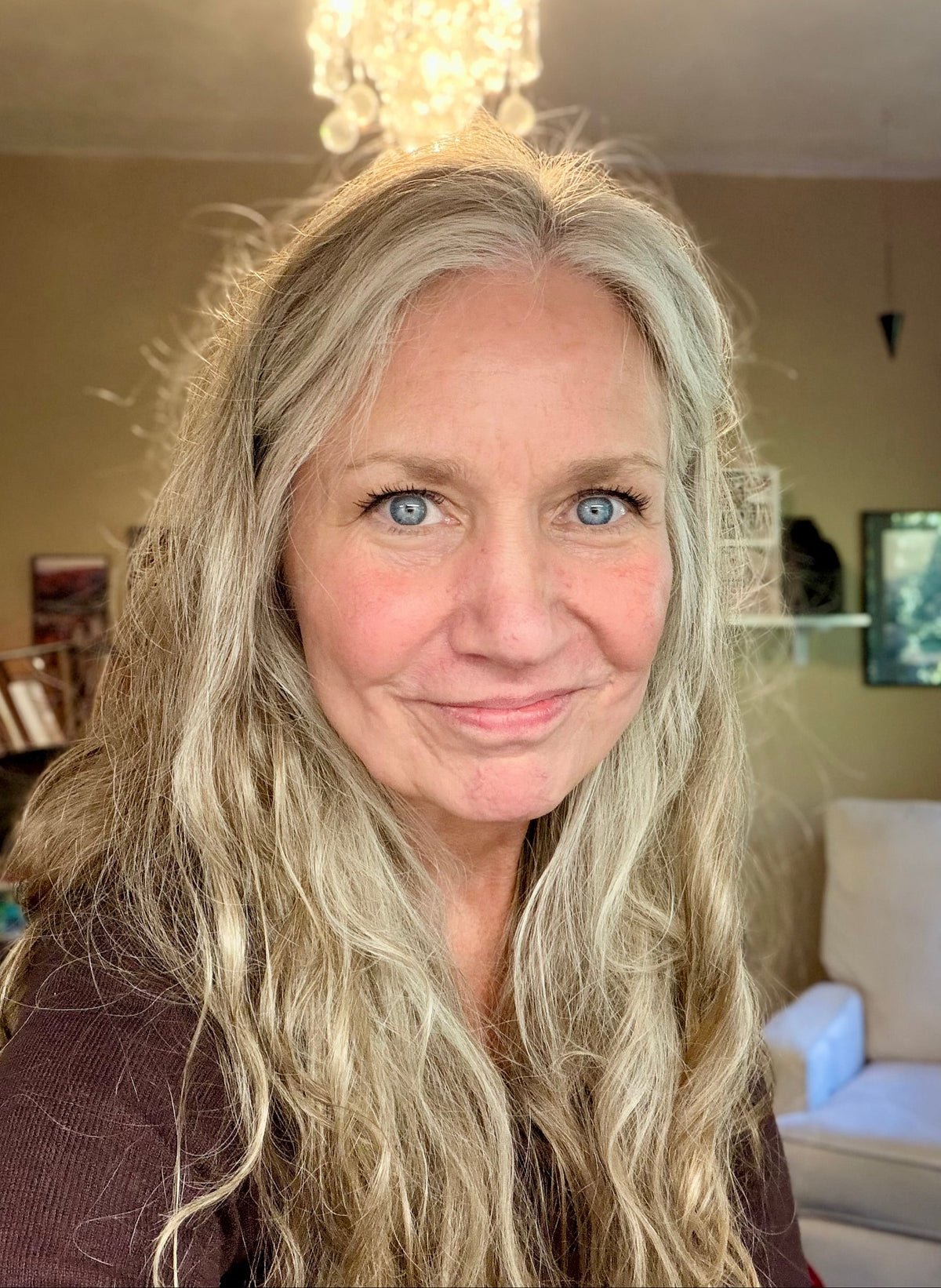 Photo of smiling blond woman in a room with a comfortable chair in the background.