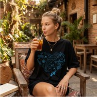 Woman sitting outdoors drinking a beverage with a straw, wearing a black t-shirt with a blue sea life graphic design.