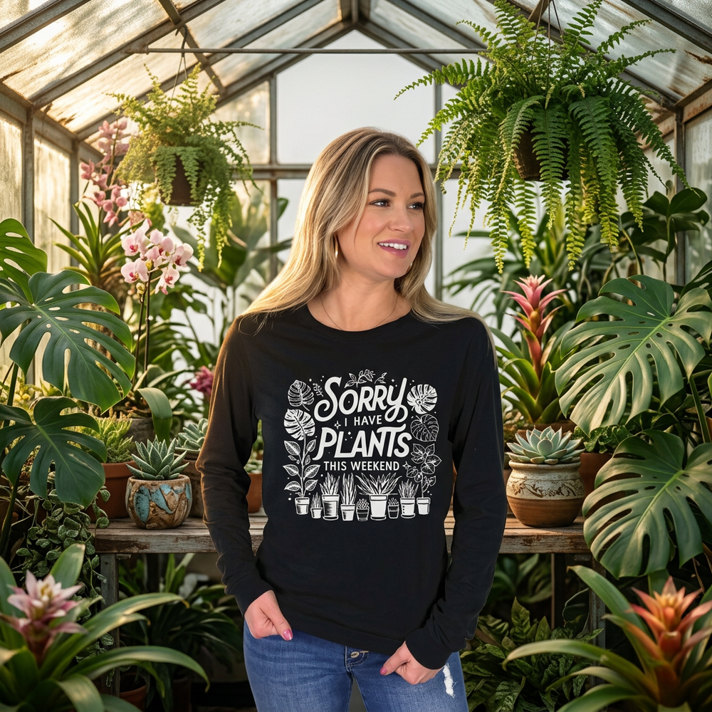 Woman standing in a greenhouse, wearing black long sleeve tee with "Sorry I have plants this weekend" graphic.