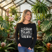 Woman standing in a greenhouse, wearing black long sleeve tee with "Sorry I have plants this weekend" graphic.