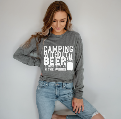 Smiling woman in light grey long sleeve tee with white graphic: “Camping without beer is just sitting in the woods”.