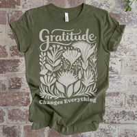 Green t-shirt with 'Gratitude Changes Everything' design on a brick background