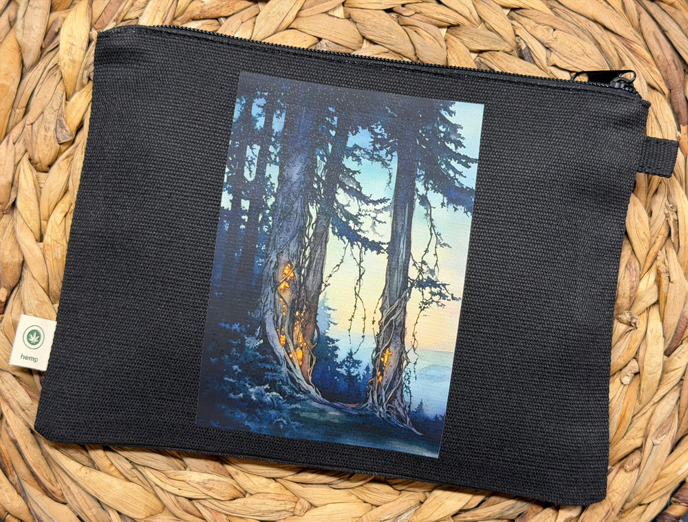A black canvas zipper pouch featuring a printed vertical art panel of a forest scene with tall trees and warm glowing trunks, displayed on a woven straw mat.