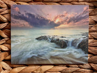 Greeting card with a dramatic ocean scene with rocky coastline and sunset, on a woven mat background