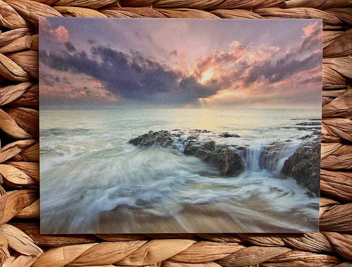 Greeting card with a dramatic ocean scene with rocky coastline and sunset, on a woven mat background