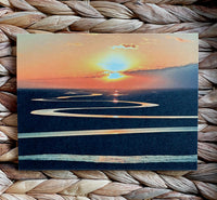 A card with a winding ribbon of river at sunset on a woven mat background.