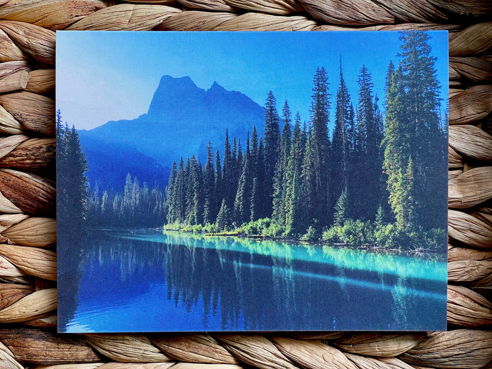 Scenic card  with a mountain and forest reflection in water, on a woven surface