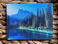 Scenic card  with a mountain and forest reflection in water, on a woven surface