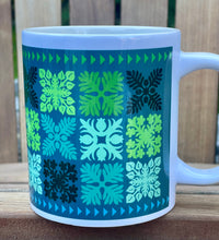 Mug with a blue and green geometric Hawaiian quilt pattern on a wooden surface