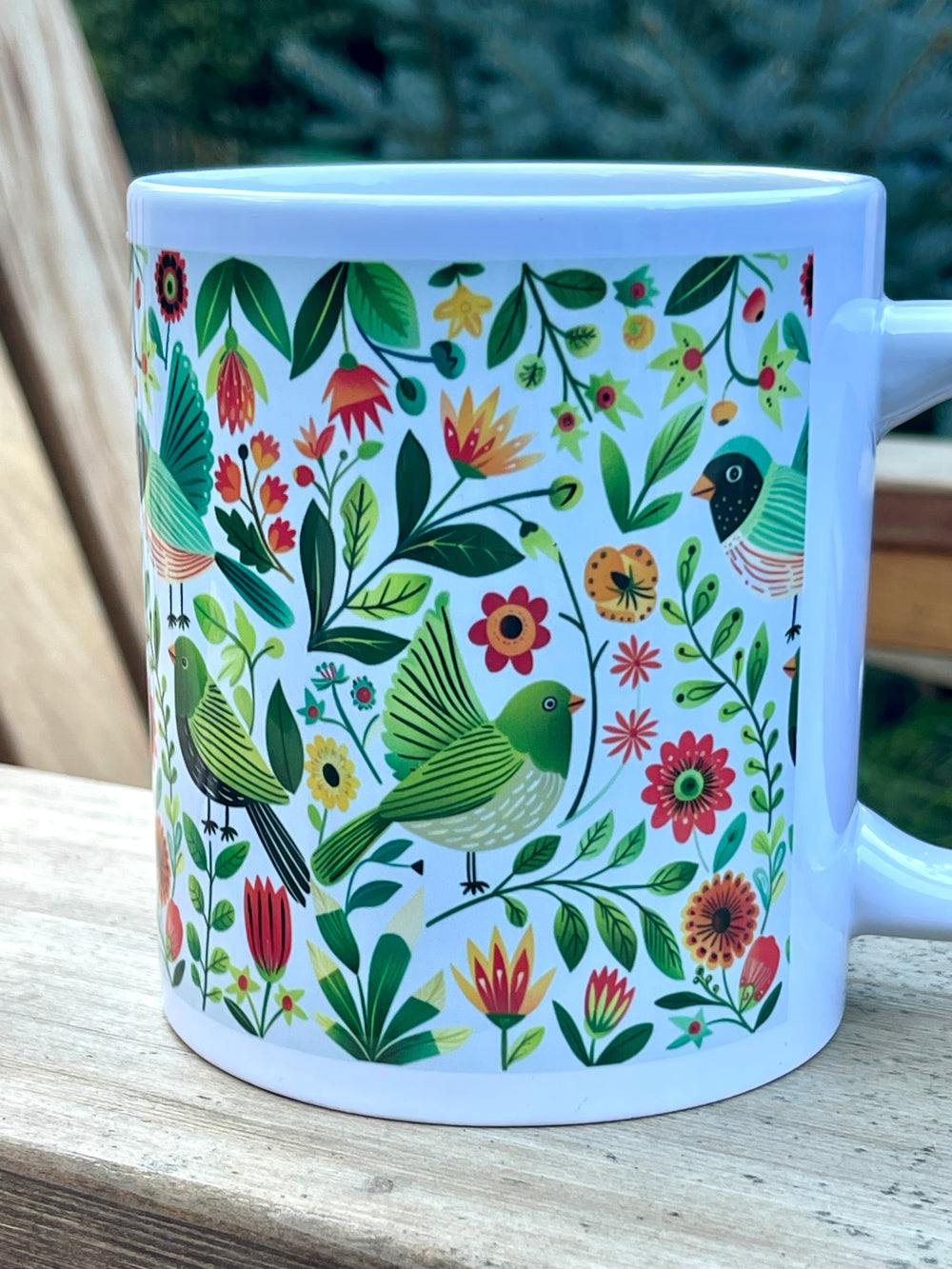 White mug with colorful bird and floral pattern on a wooden surface