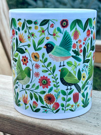 Ceramic mug with colorful bird and floral pattern on a wooden surface
