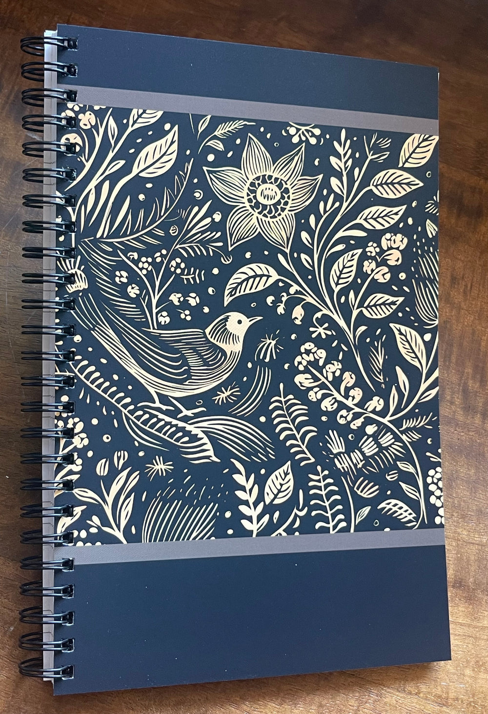 Spiral-bound notebook with black and beige illustration of a bird and flowers.