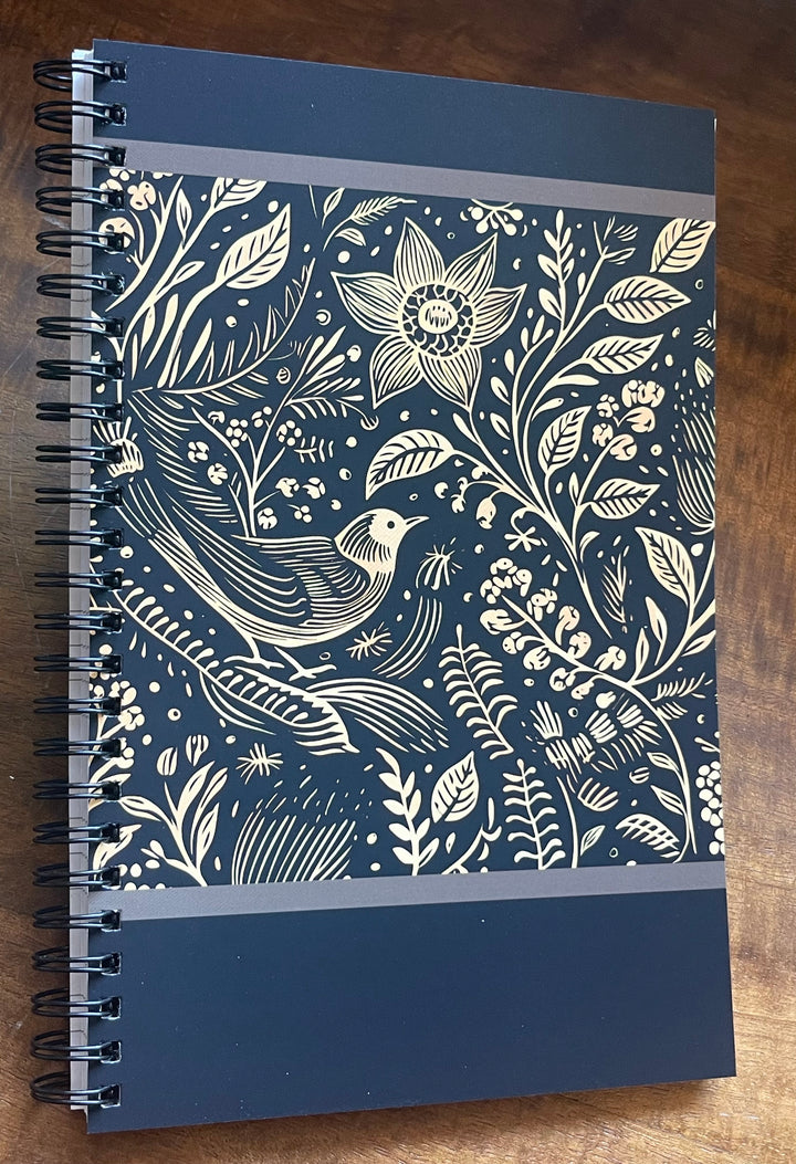 Spiral-bound notebook with black and beige illustration of a bird and flowers.