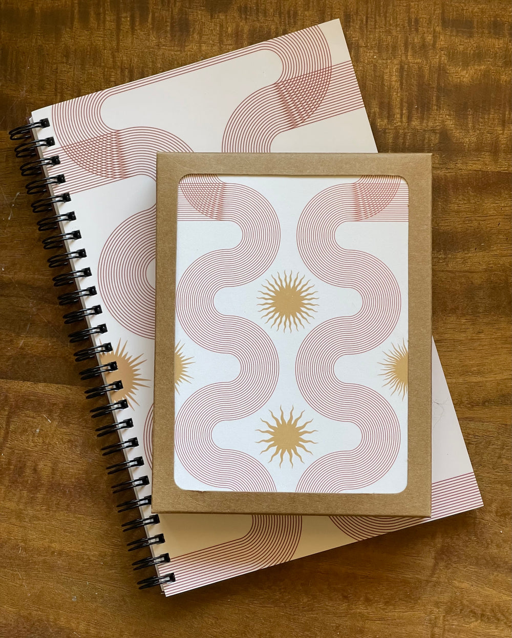 A box of greeting cards featuring abstract linear artwork, stacked on top of a matching spiral-bound notebook.