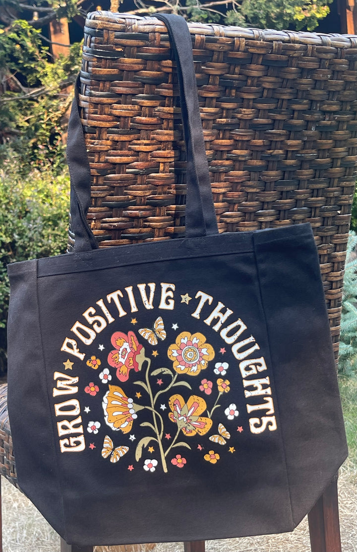 Black tote bag with flowery “Grow Positive Thoughts” graphic.