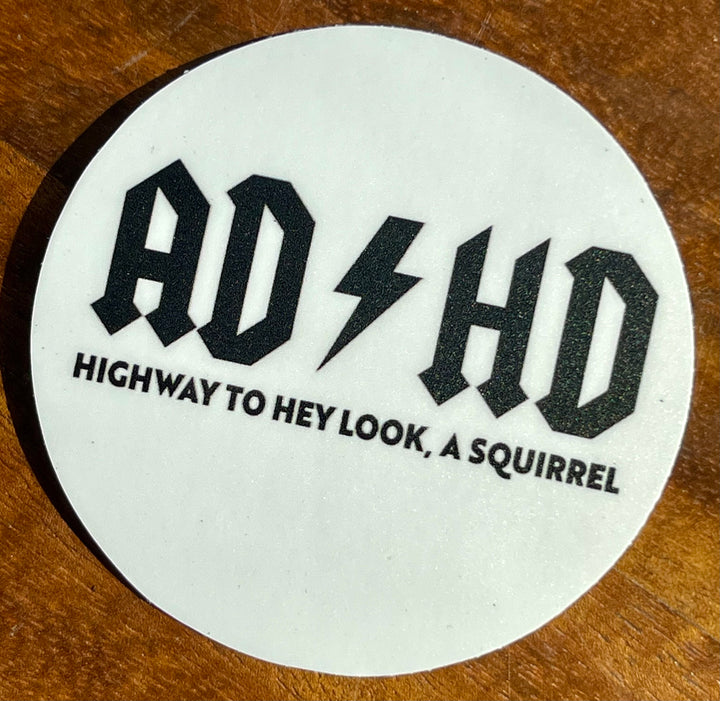 Three-inch sticker, white background, black text. Has “ADHD” in style of AC/DC’s iconic logo, with tagline of “Highway to hey look, a squirrel”.