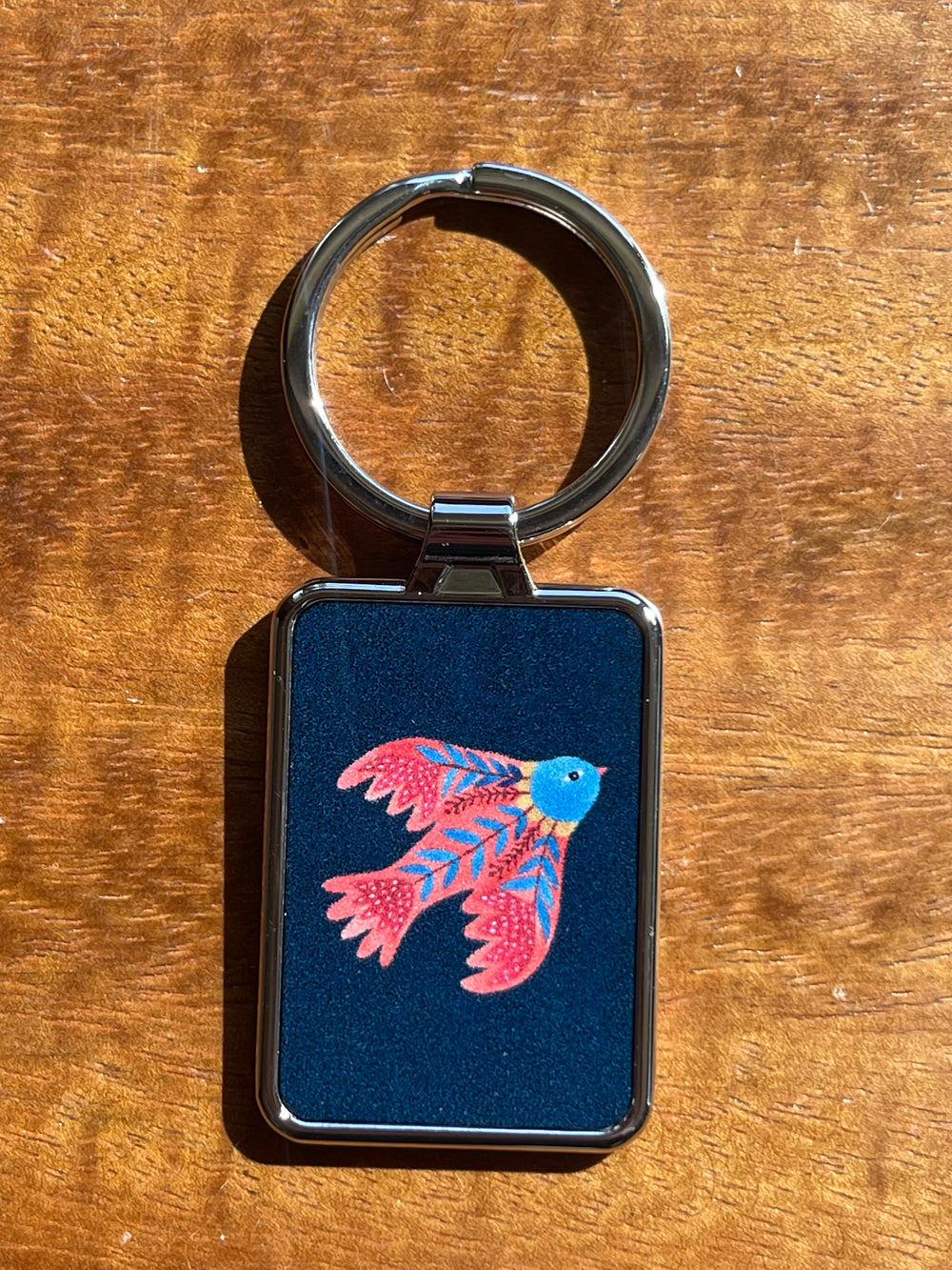 Keychain with a colorful red bird design on a blue background, placed on a wooden surface.