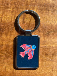 Keychain with a colorful red bird design on a blue background, placed on a wooden surface.