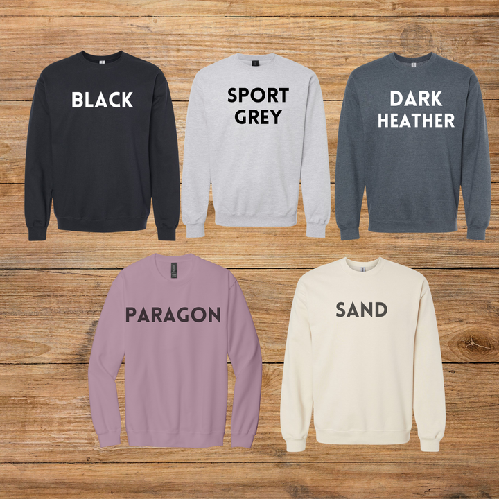 Five sweatshirts in different colors with text labels on a wooden background