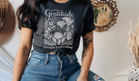 Person wearing a black t-shirt with 'Gratitude Changes Everything' design, sitting indoors.